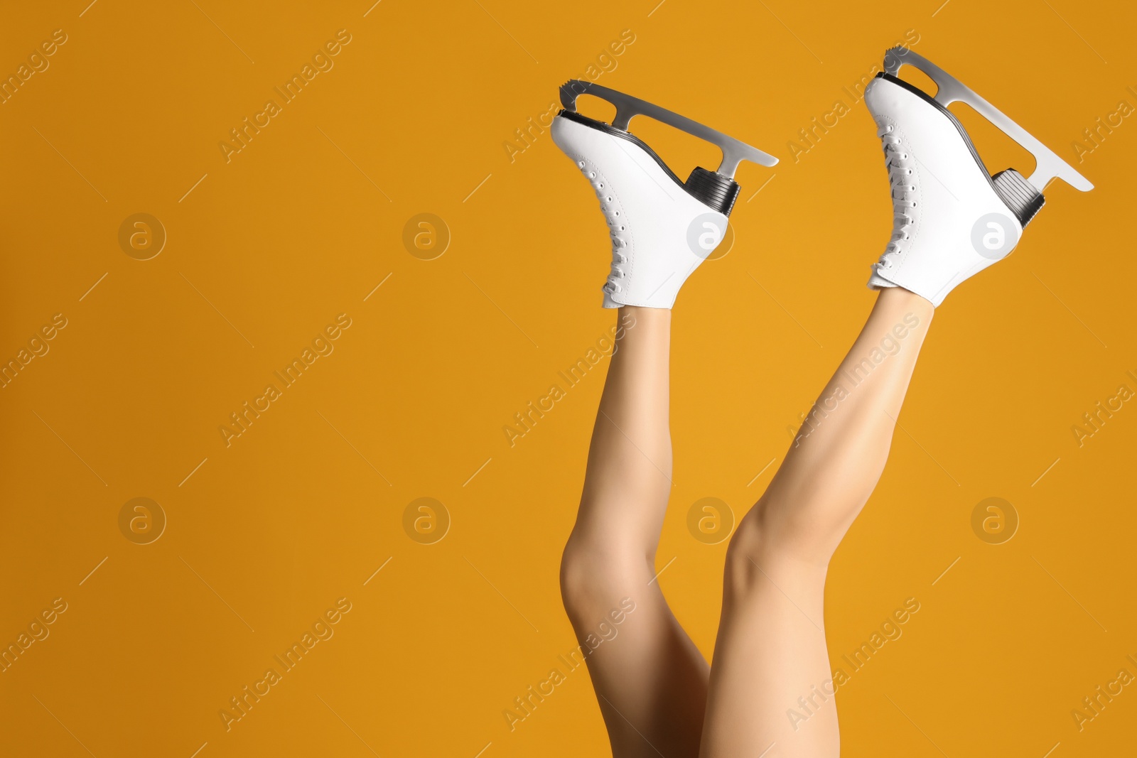 Photo of Woman in elegant white ice skates on yellow background, closeup of legs. Space for text