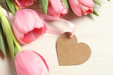 Happy Mother's Day. Beautiful pink tulips with blank heart shaped card on white wooden table, flat lay