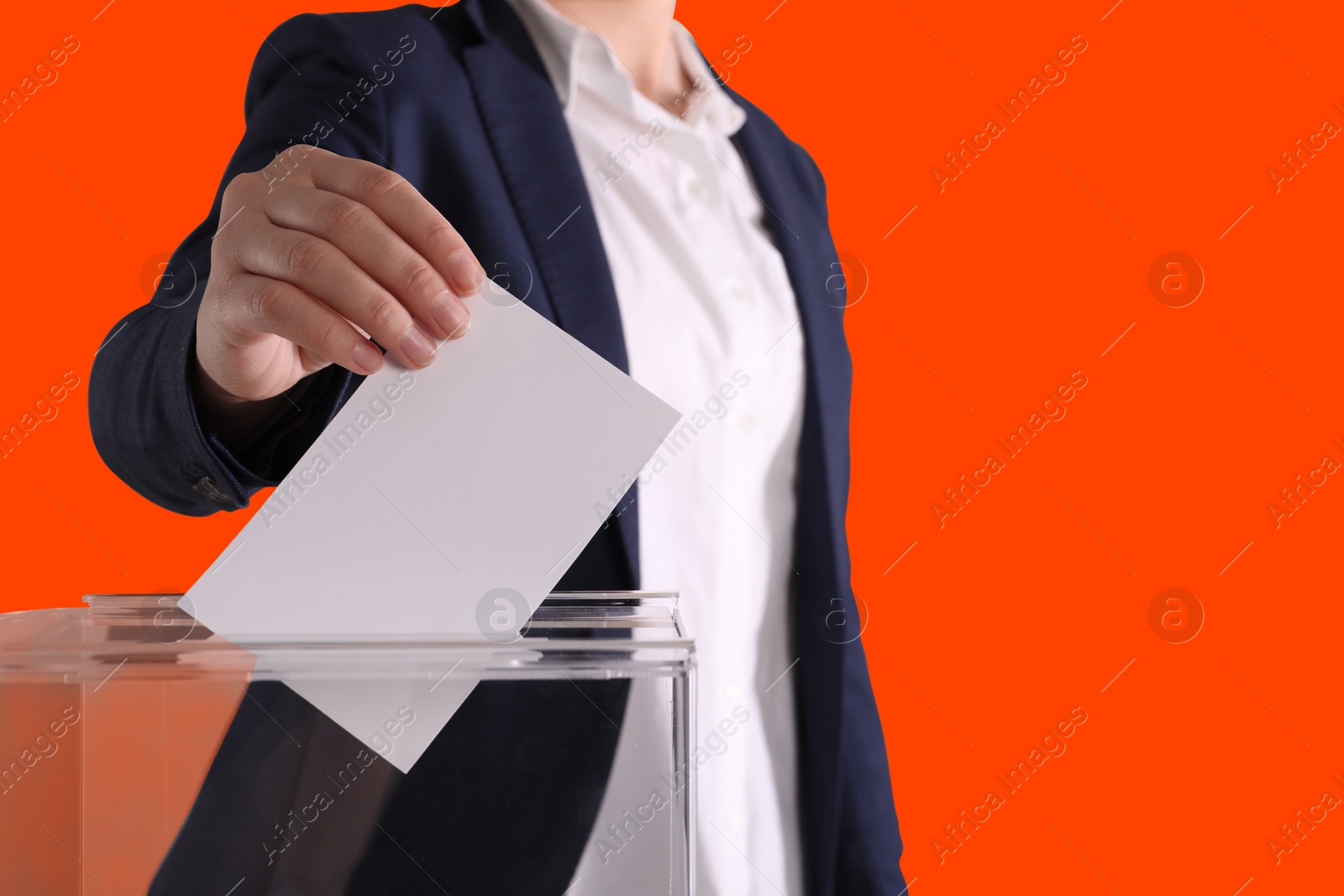 Image of Woman putting her vote into ballot box on dark orange background, closeup