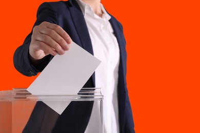 Image of Woman putting her vote into ballot box on dark orange background, closeup