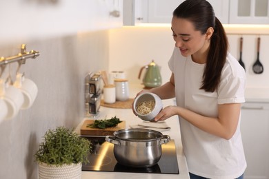 Smiling woman adding noodles into pot with soup in kitchen