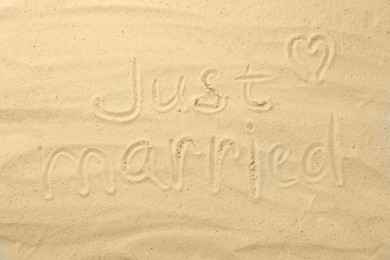 Photo of Honeymoon concept. Phrase Just married and heart written on sand, top view