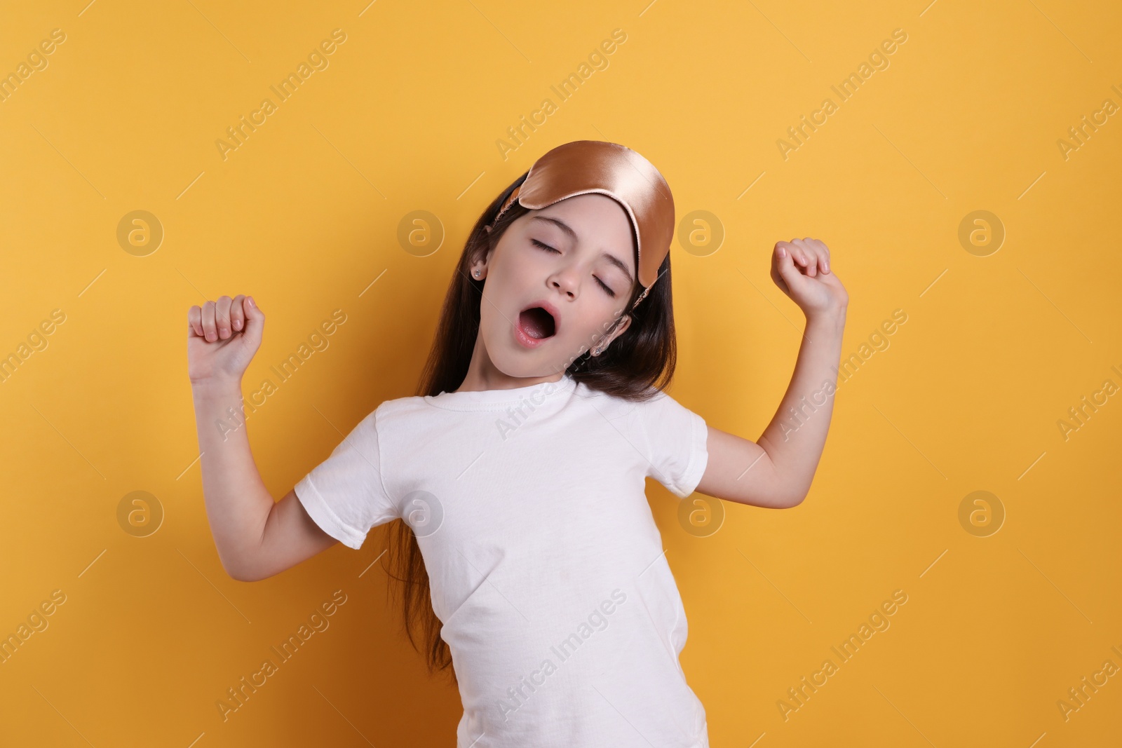 Photo of Tired little girl with sleep mask yawning on yellow background