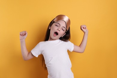 Photo of Tired little girl with sleep mask yawning on yellow background