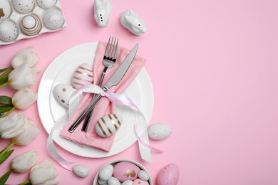 Photo of Festive table setting with painted eggs and tulips on pink background, flat lay with space for text. Easter celebration
