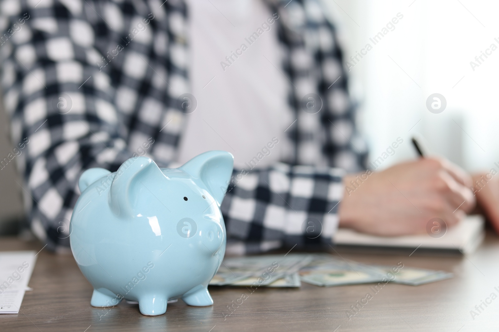 Photo of Financial savings. Man writing down notes at wooden table, focus on piggy bank