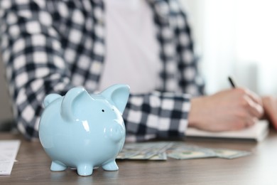 Financial savings. Man writing down notes at wooden table, focus on piggy bank