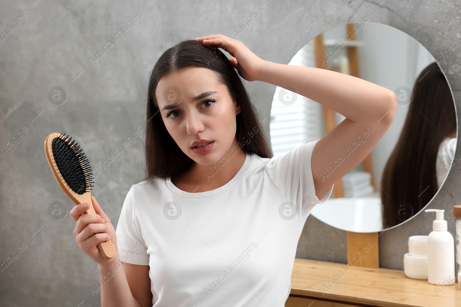 Photo of Emotional woman with brush examining her hair at home. Dandruff problem