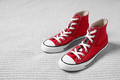 Photo of Pair of new stylish red sneakers on light grey fabric. Space for text