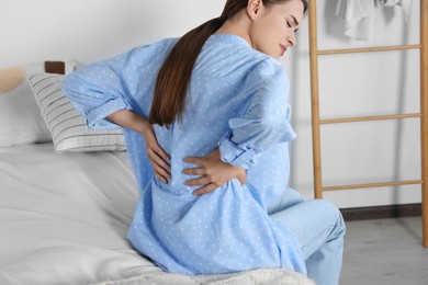 Photo of Woman suffering from back pain while sitting on bed at home. Symptom of scoliosis