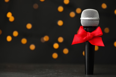 Photo of Microphone with red bow on table against blurred lights, space for text. Christmas music