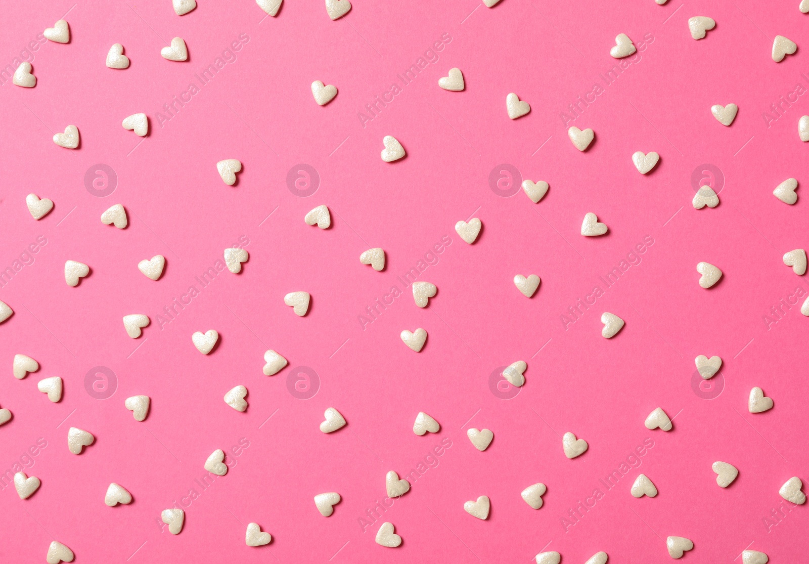 Photo of White heart shaped sprinkles on pink background, flat lay