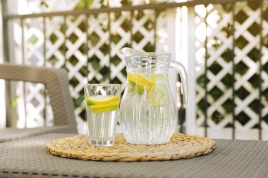 Photo of Glass and jug of water with lemons on table outdoors