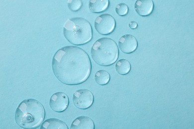 Photo of Drops of cosmetic serum on light blue background, top view. Space for text