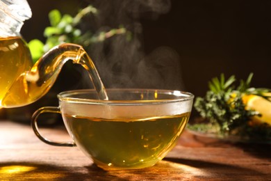 Photo of Pouring aromatic herbal tea into cup on wooden table, closeup