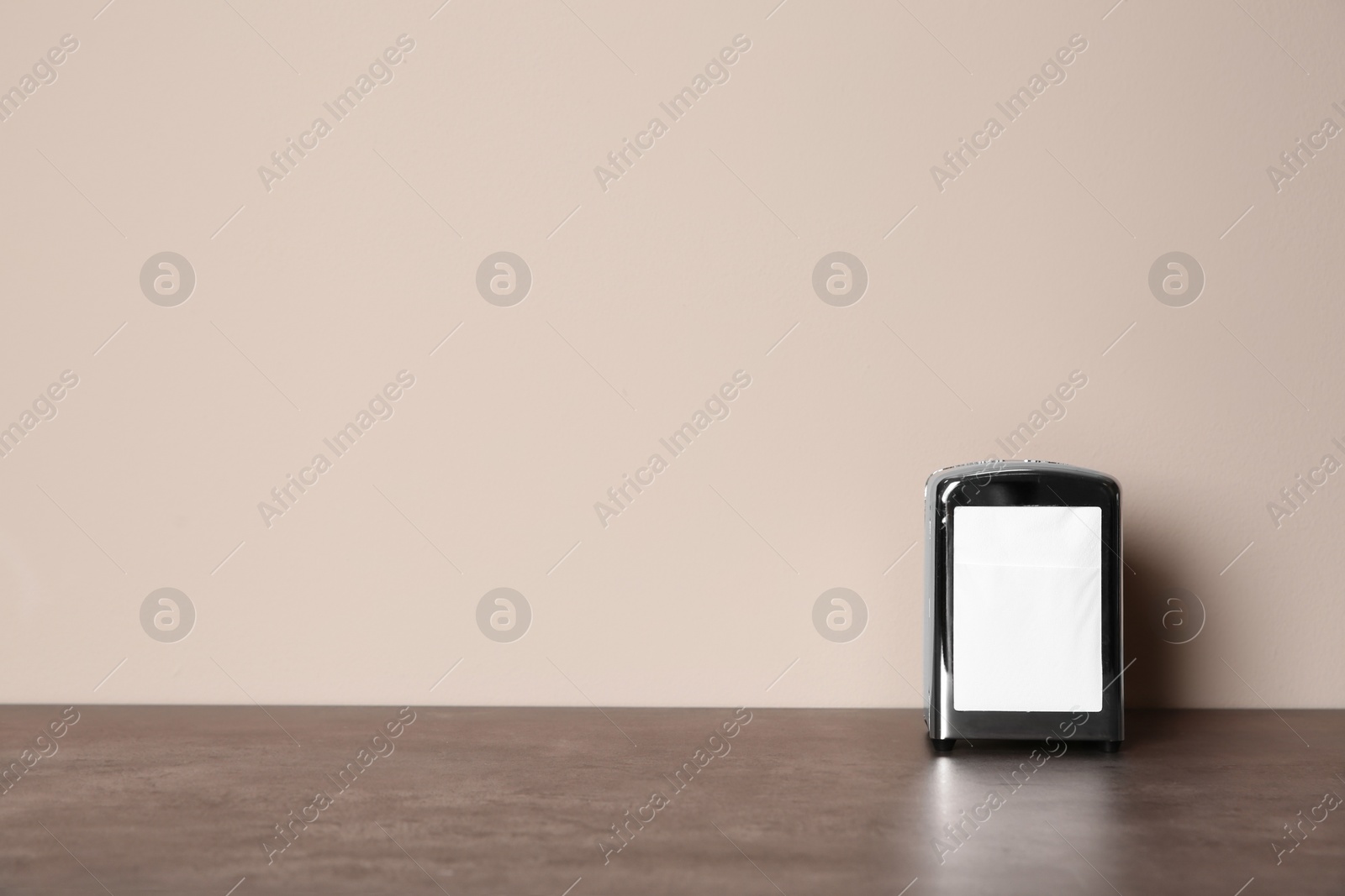 Photo of Napkin holder with paper serviettes on table against color background. Space for text