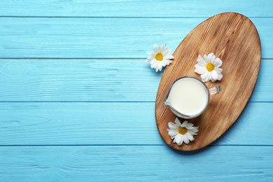 Jug with milk and flowers on color wooden background, top view