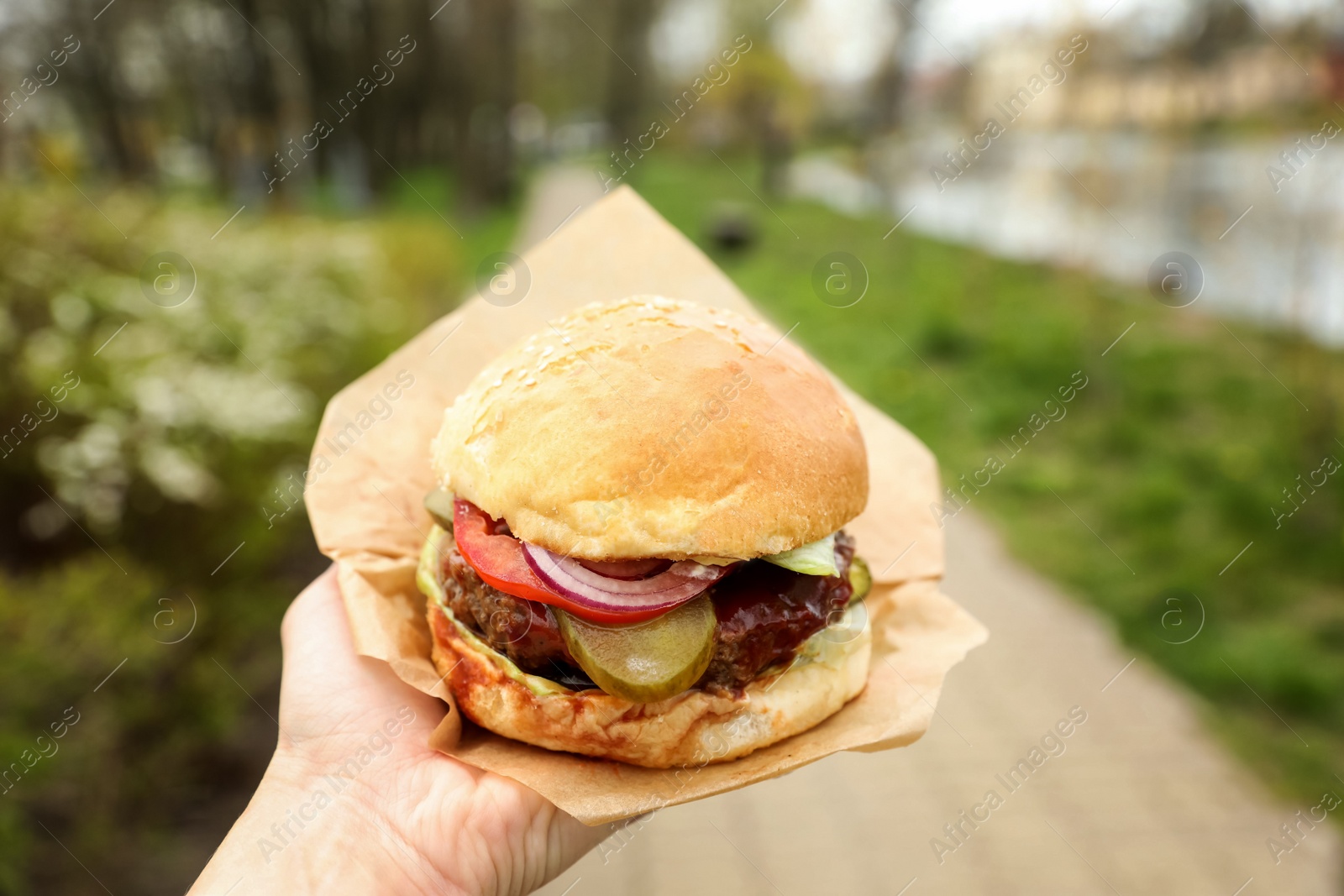 Photo of Little girl holding fresh delicious burger outdoors, closeup. Street food