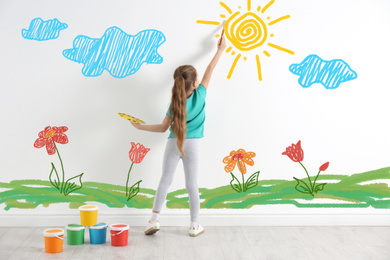 Cute child drawing nature on white wall indoors