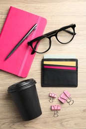 Photo of Leather business card holder with colorful cards, stationery, glasses and coffee on wooden table, flat lay