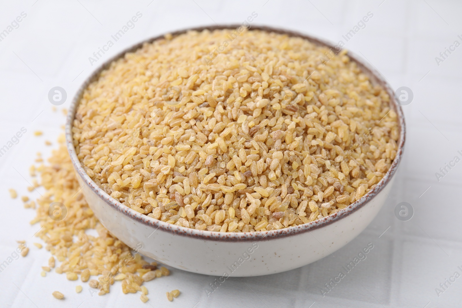 Photo of Raw bulgur in bowl on white table, closeup