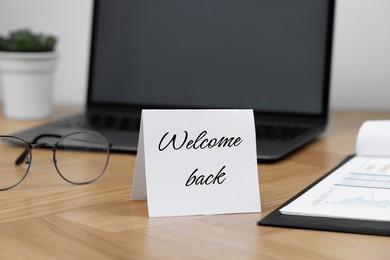 Paper note with phrase Welcome Back on office desk