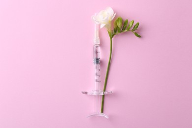 Cosmetology. Medical syringe and freesia flower on pink background, top view