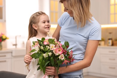 Little daughter congratulating her mom with bouquet of alstroemeria flowers in kitchen. Happy Mother's Day