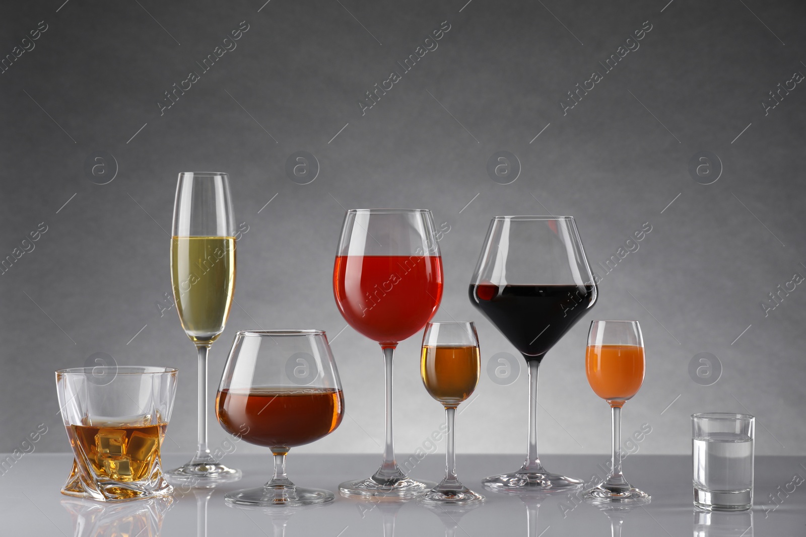 Photo of Glasses with different alcoholic drinks on table against gray background