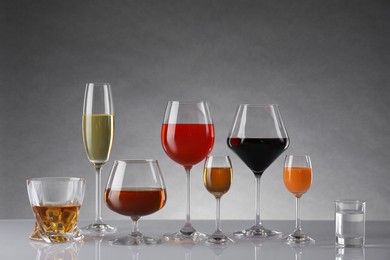 Glasses with different alcoholic drinks on table against gray background