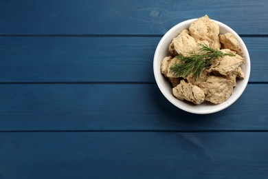 Photo of Dehydrated soy meat chunks with dill in bowl on blue wooden table, top view. Space for text