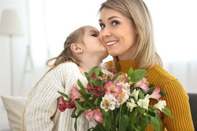 Little daughter kissing and congratulating her mom with bouquet of alstroemeria flowers at home. Happy Mother's Day