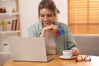 Photo of Woman with credit cards using laptop for online shopping at wooden table indoors