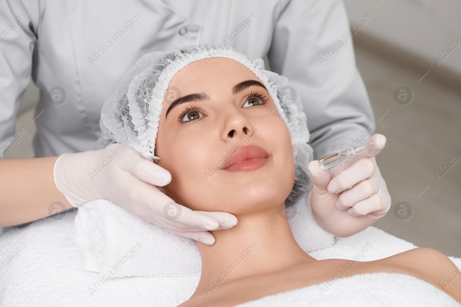 Photo of Professional cosmetologist holding skincare ampoule while working with client in clinic, closeup