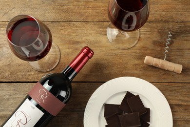Photo of Flat lay composition with tasty red wine and chocolate on wooden table