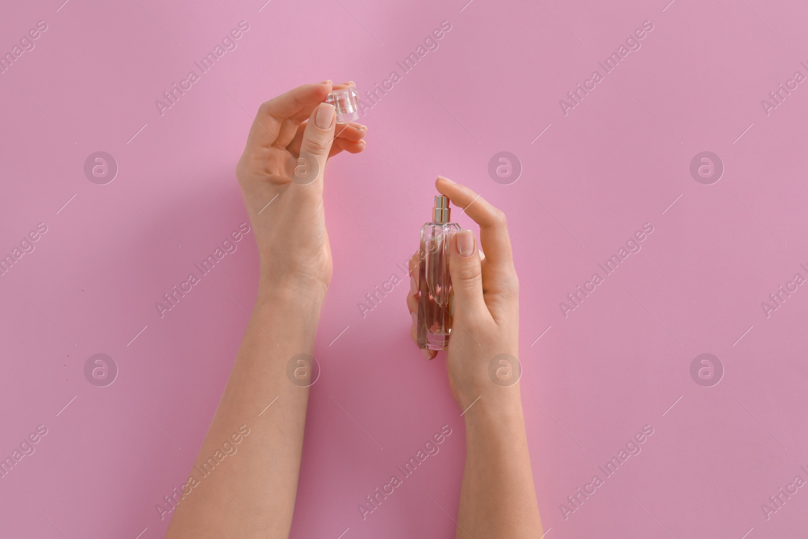 Photo of Woman applying perfume on pink background, top view