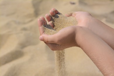 Photo of Child pouring sand from hands outdoors, closeup. Fleeting time concept