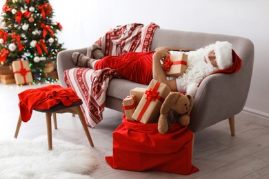 Photo of Authentic Santa Claus with gift sleeping on sofa indoors