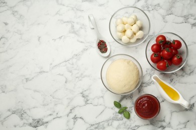 Raw pizza dough and other ingredients on white marble table, flat lay. Space for text
