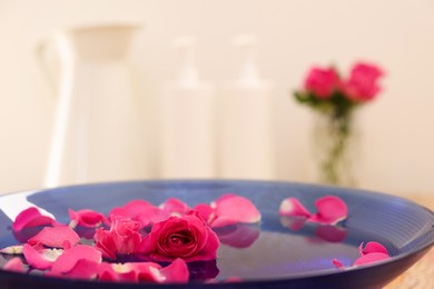 Photo of Pink rose and petals in bowl with water on table, closeup. Space for text