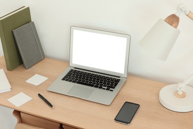 Image of Comfortable workplace at home. Modern laptop with blank screen and lamp on wooden desk. Mockup for design