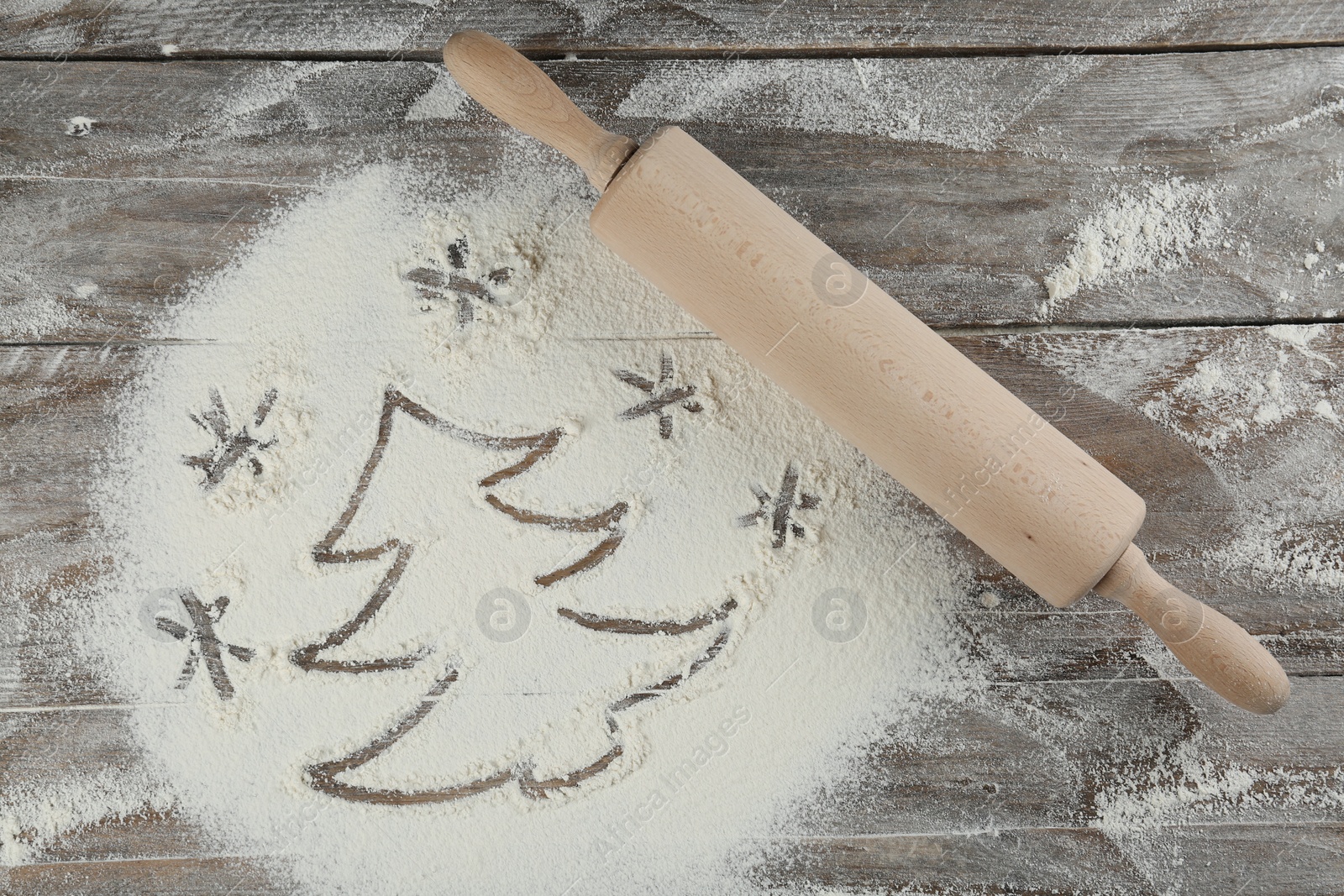 Photo of Christmas tree and snowflakes made of flour near rolling pin on wooden table, top view