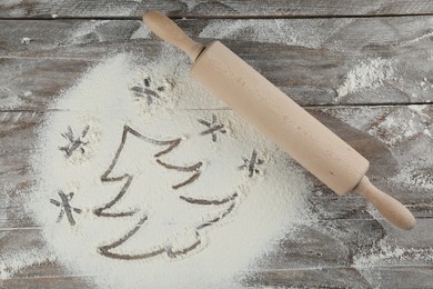 Photo of Christmas tree and snowflakes made of flour near rolling pin on wooden table, top view