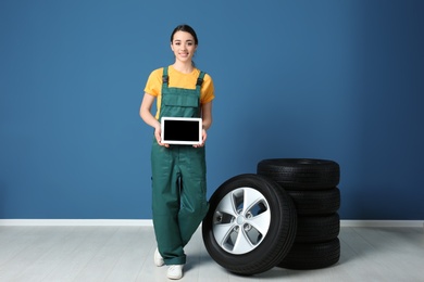 Photo of Female mechanic in uniform with car tires and tablet computer on color wall background