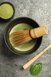 Photo of Cup of fresh matcha tea with bamboo whisk, spoon and green powder on grey table, flat lay