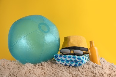 Photo of Beach ball and other accessories on sand against yellow background