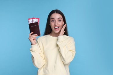 Happy woman with passport and tickets on light blue background