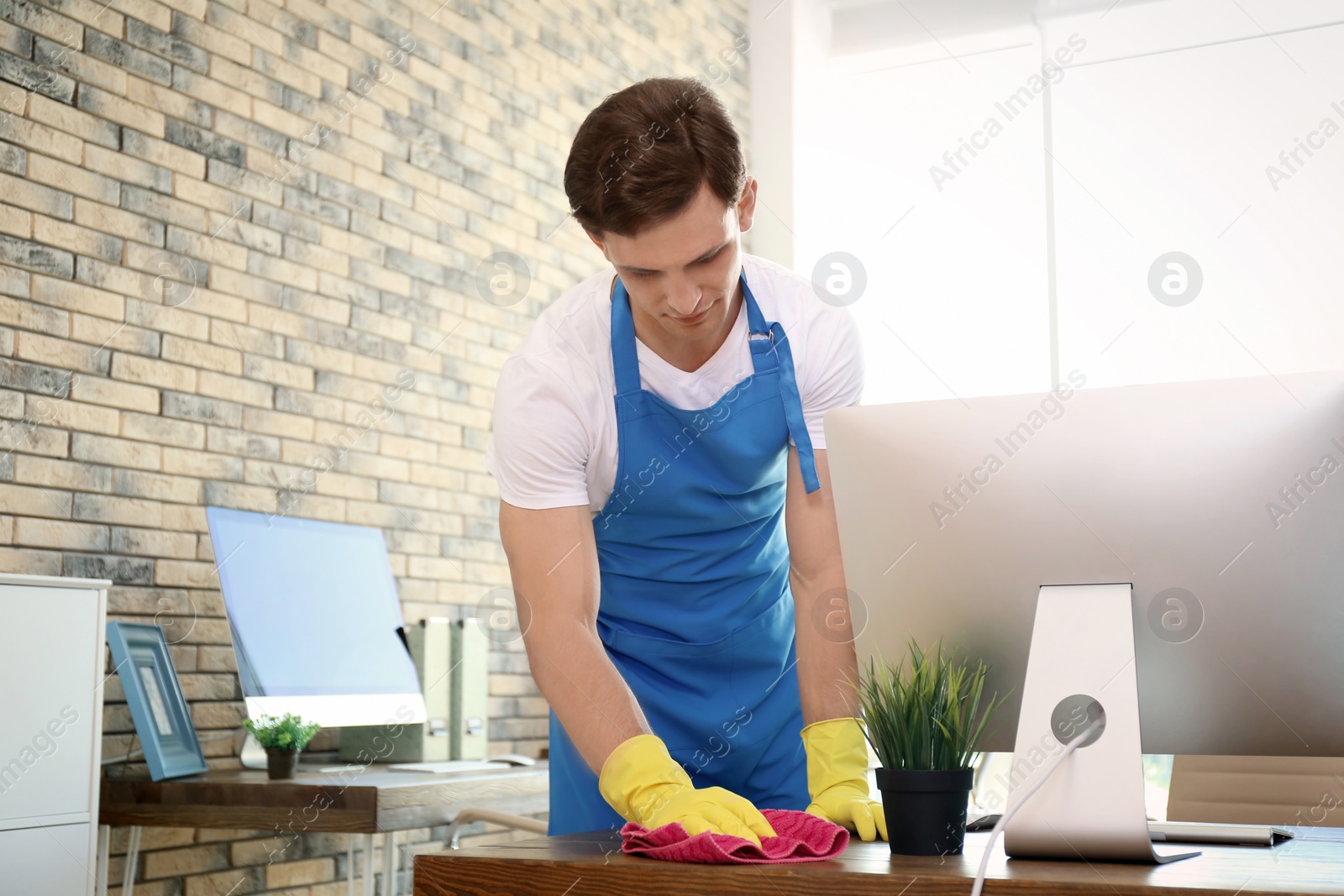 Photo of Young man in apron and gloves cleaning office
