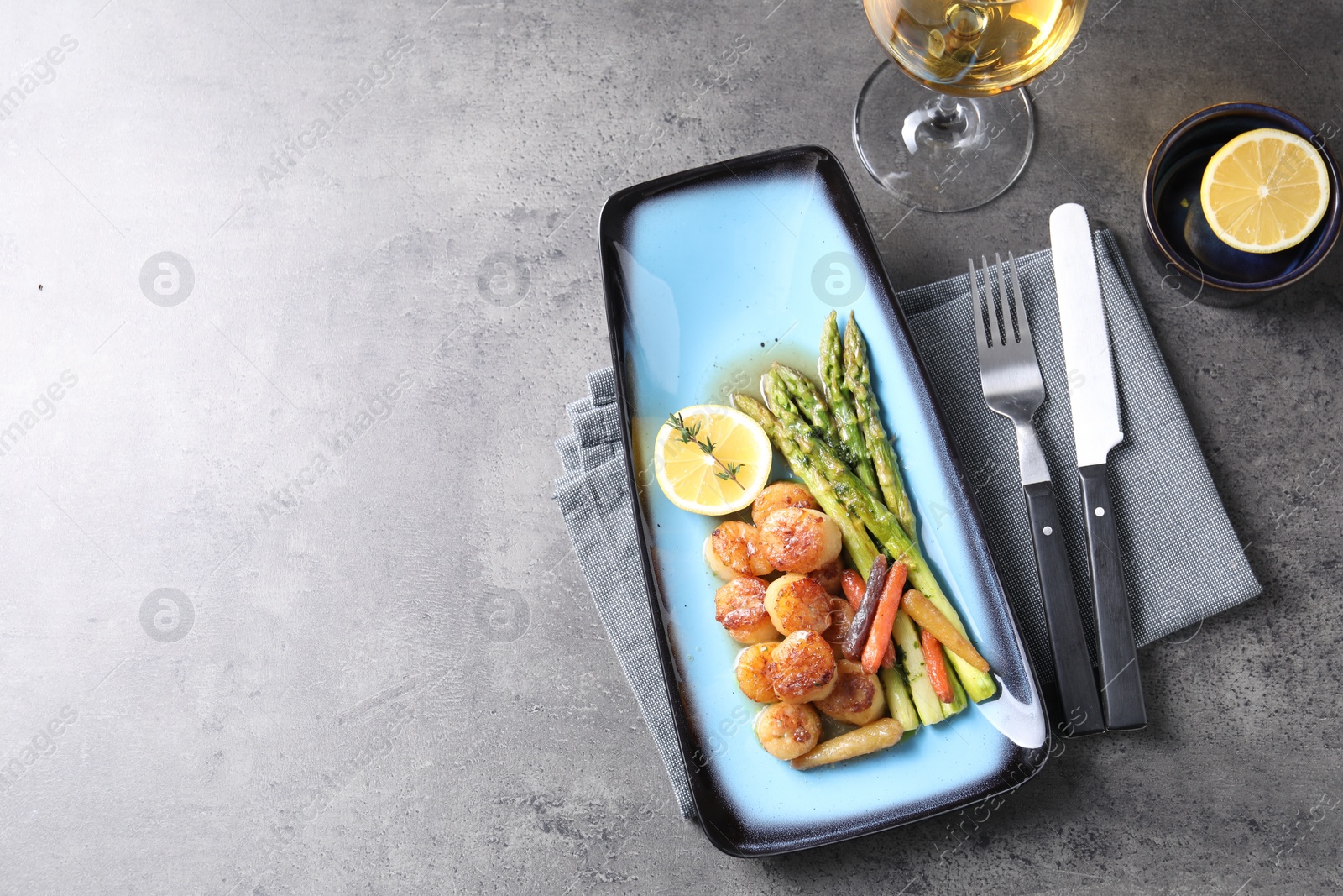 Photo of Delicious fried scallops with asparagus served on grey table, flat lay. Space for text