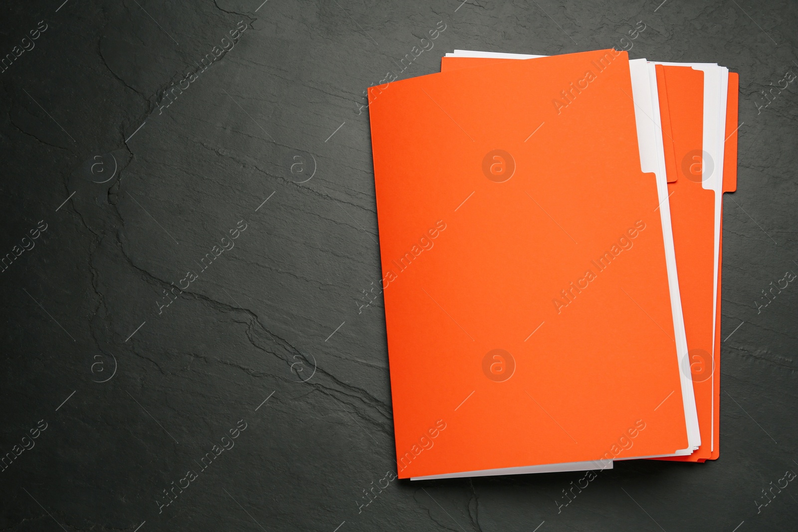 Photo of Orange files with documents on black slate table, top view. Space for text